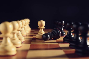 Satranç tahtasındaki siyah ve beyaz piyonlar karanlık arka plana karşı, yakın plan. Rekabet konsepti