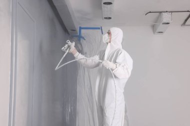 Dekoratör duvarları gri renge boyuyor ve kapalı alanda sprey boyayla boyuyor.