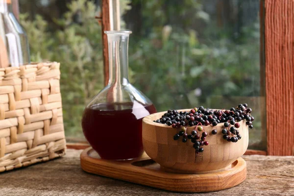 窓の近くの木製のテーブルの上にサンブカスの果実とエルダーベリーワインとボウル — ストック写真