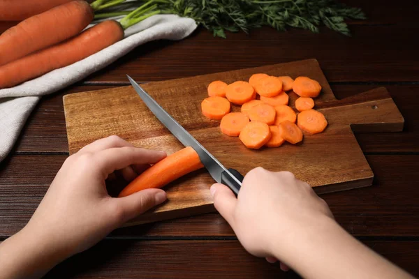 Woman Cutting Tasty Carrot Brown Wooden Table Closeup — Stockfoto