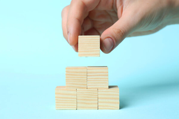 Woman building pyramid of cubes on light blue background, closeup with space for text. Idea concept
