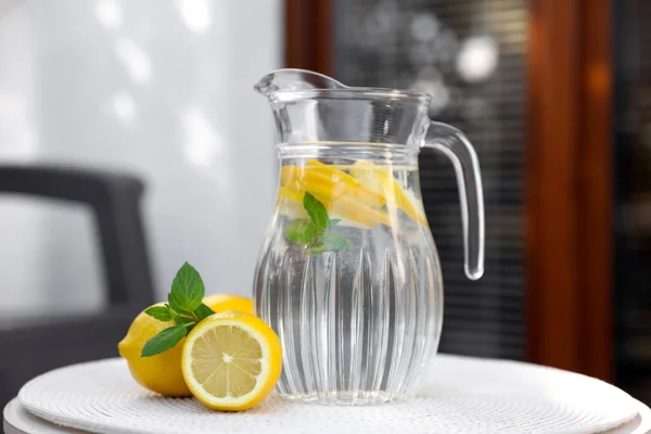 屋外の白いテーブルの上にレモンとミントと水のジャグ — ストック写真