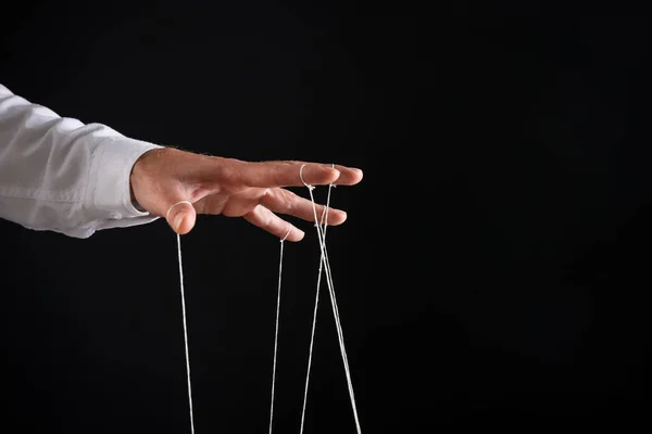 Man pulling strings of puppet on black background, closeup. Space for text