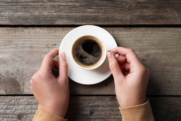 木のテーブルで熱い香りのコーヒーのカップを持つ女性 トップビュー — ストック写真