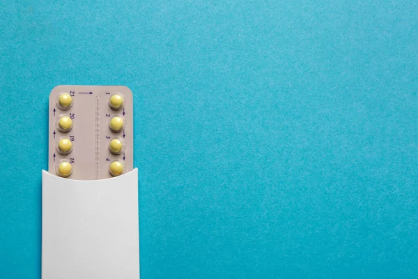 Birth control pills on light blue background, top view. Space for text