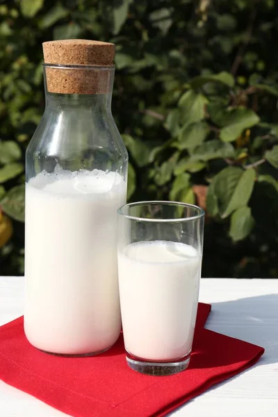 屋外の白い木製のテーブルの上に新鮮な牛乳のガラスとボトル — ストック写真
