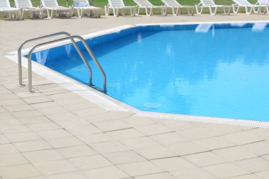 Güneşli bir günde tatil köyünde tırabzanları olan açık havuz.