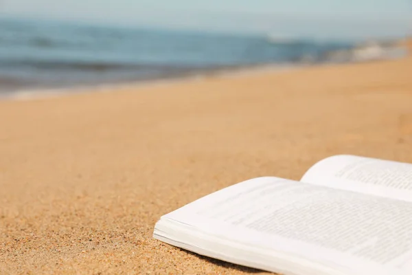 stock image Open book on sandy beach near sea, closeup. Space for text