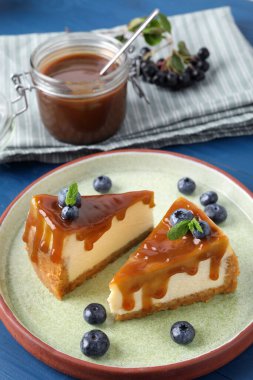 Pieces of delicious caramel cheesecake with blueberry and mint on blue wooden table