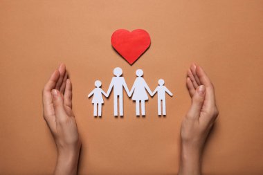 Kâğıt aile figürlerini koruyan kadın ve kahverengi arka planda kırmızı kalp. Sigorta konsepti