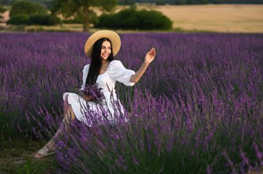 Beautiful young woman with bouquet sitting in lavender field