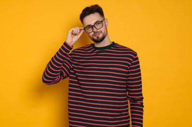 Sarı arka planda çizgili sweatshirt ve gözlüklü yakışıklı bir adam.