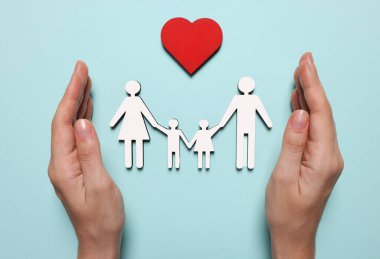 Açık mavi arka planda aile ve kalp figürlerini koruyan bir kadın. Sigorta konsepti