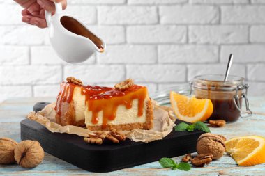 Woman pouring caramel sauce onto delicious pieces of cheesecake at wooden table, closeup