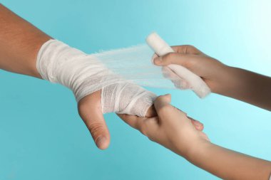 Doktor açık mavi arka planda hastanın eline bandaj uyguluyor.