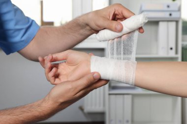 Doctor applying bandage onto patient's wrist in hospital, closeup