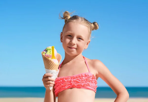 夏の晴れた日にビーチでおいしいアイスクリームと水着の愛らしい女の子 — ストック写真