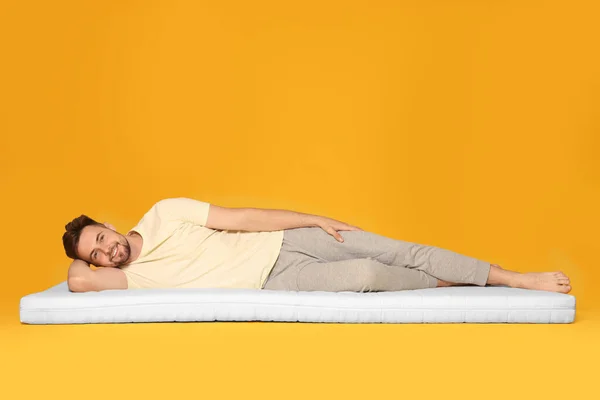 Lächelnder Mann Liegt Auf Weicher Matratze Vor Orangefarbenem Hintergrund — Stockfoto