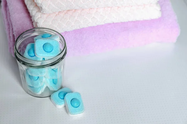 Jar with water softener tablets near stacked towels on table, space for text