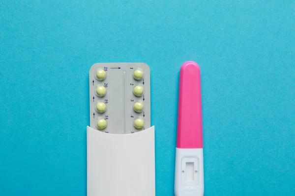 Birth control pills and pregnancy test on light blue background, top view. Space for text