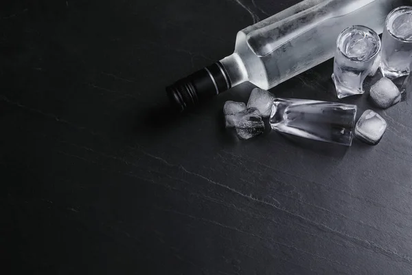 ウォッカのボトルと黒のテーブルの上に氷とショットグラス フラットレイ テキストのスペース — ストック写真