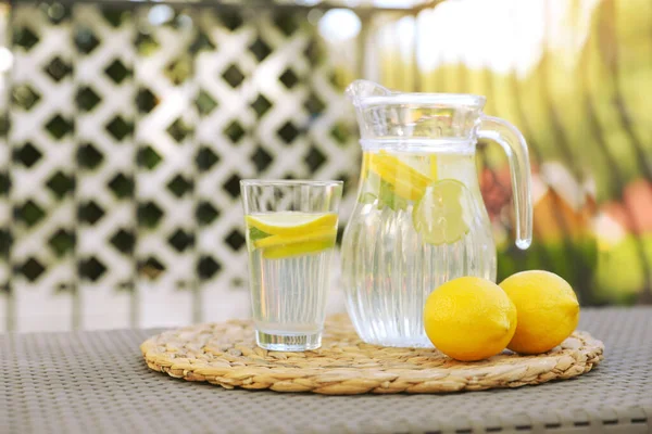 屋外のテーブルの上にレモンと水のガラスとジャグ — ストック写真