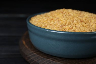 Bir kase pişmemiş bulgur siyah ahşap masada, yakın plan.