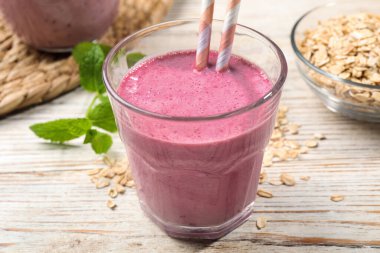 Bir bardak böğürtlenli smoothie, pipetli, nane ve yulaf ezmeli ahşap masa, yakın plan.