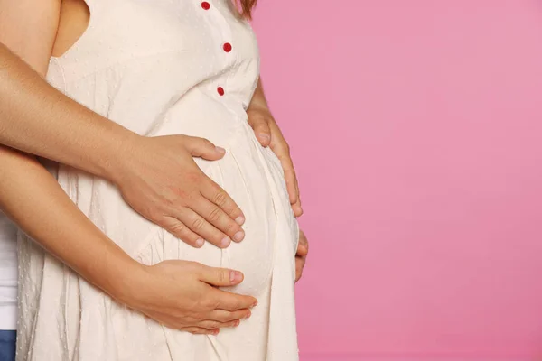 男人抱着他怀孕的妻子粉红的背景 案文的篇幅 — 图库照片
