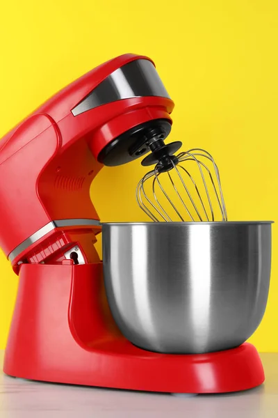 Modern red stand mixer on white wooden table against yellow background