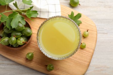 Tasty gooseberry juice and fresh berries on light wooden table, flat lay clipart