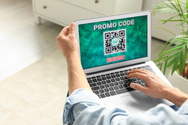 Kapalı mekanda aktif promosyon kodlu dizüstü bilgisayar tutan adam.