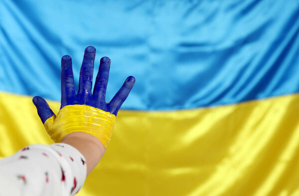 Little girl with paint on hand near Ukrainian flag, closeup. Space for text