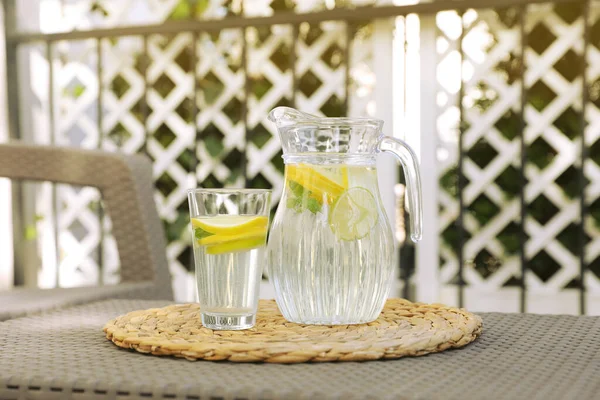 屋外のテーブルの上にレモンと水のガラスとジャグ — ストック写真