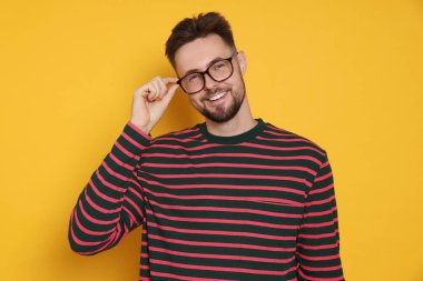 Sarı arka planda çizgili sweatshirt ve gözlüklü yakışıklı bir adam.