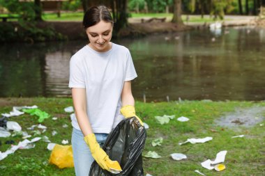 Plastik çantalı genç bir kadın parkta çöp topluyor.