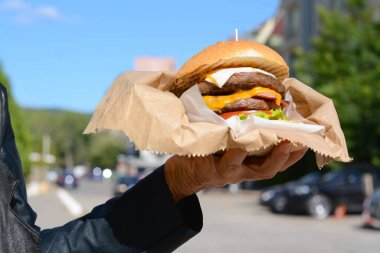 Lezzetli hamburgerleri kağıtta tutan kadın şehir caddesinde, yakın plan.
