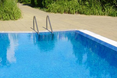 Outdoor swimming pool with ladder and handrails on sunny day