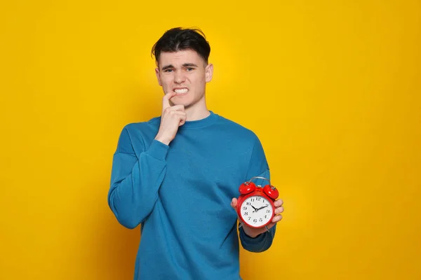 Emotional young man with alarm clock on orange background. Being late concept