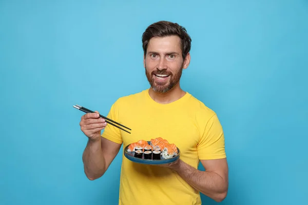 Šťastný Muž Drží Talíř Chutnými Sushi Rolky Hůlky Světle Modrém — Stock fotografie