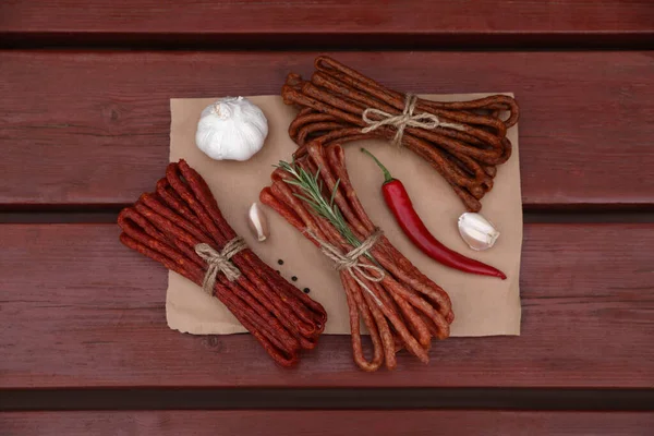 stock image Bundles of delicious kabanosy with rosemary, peppercorn, garlic and chilli on wooden table, top view