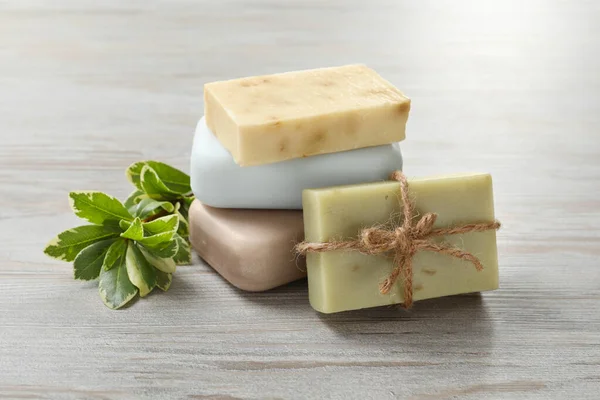 Stack of different soap bars and green plant on white wooden table, closeup