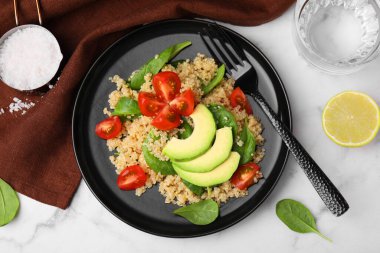 Beyaz mermer masada servis edilen domatesli nefis kinoa salatası, avokado dilimleri ve ıspanak yaprakları.