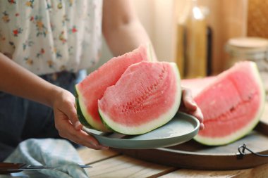 Woman holding plate with sliced fresh juicy watermelon over wooden table, closeup clipart