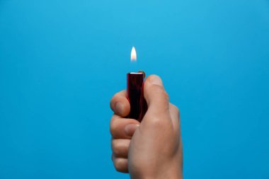 Açık mavi arka planda siyah çakmak tutan kadın, yakın plan.