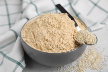 Seramik kasede susam unu, gri masada bir kaşık tohum, yakın plan.