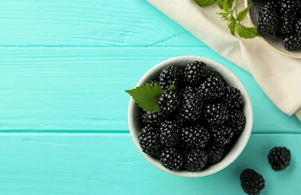 stock image Bowl of fresh ripe blackberries on turquoise wooden table, flat lay. Space for text