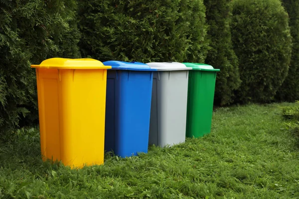 Many color recycling bins on green grass outdoors, space for text