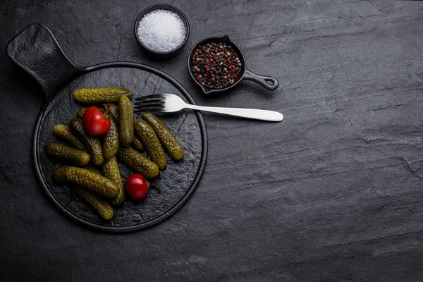 Serving board with pickled cucumbers and peppers on black table, flat lay. Space for text