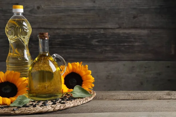 Sunflower cooking oil, seeds and yellow flowers on wooden table, space for text
